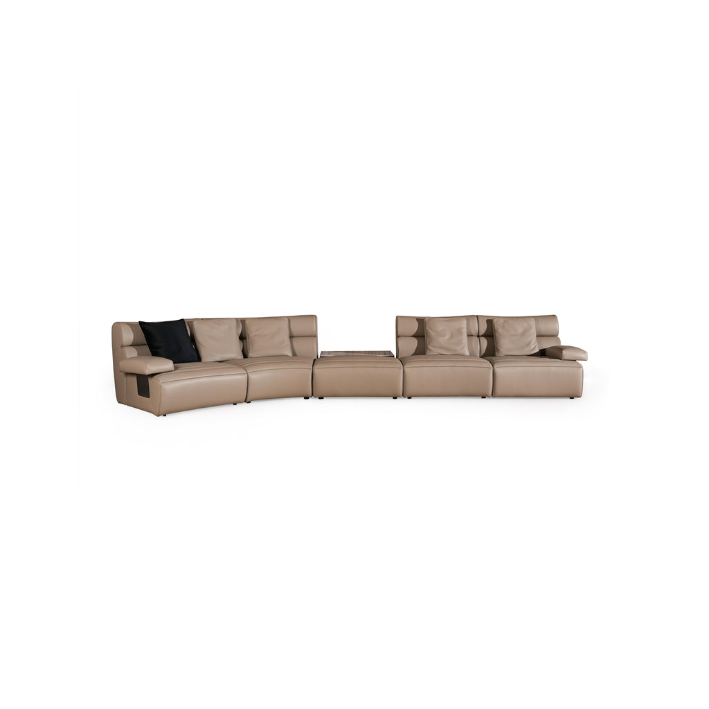 Modern sectional sofa with tan upholstery and one black cushion, featuring curved seating, segmented backrests, armrests, and low-profile legs; designed for lounging, with visible stitching and smooth surface texture. Category: furniture/sofas