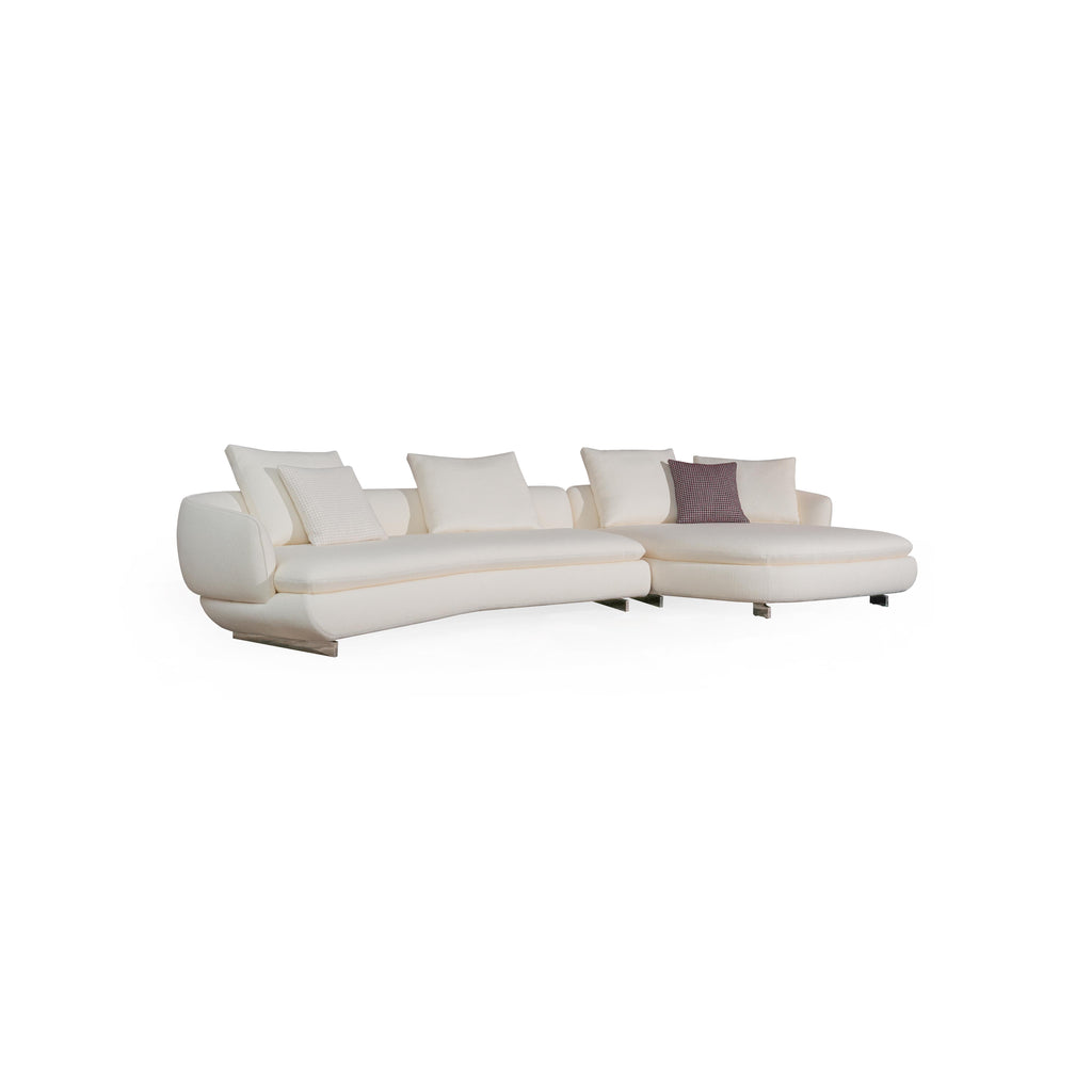 Modern sectional sofa with off-white fabric upholstery, curved backrest, padded armrests, and low-profile metal legs. Features multiple cushions, including one with a textured pattern. Designed for seating and lounging. Category: furniture/sofas