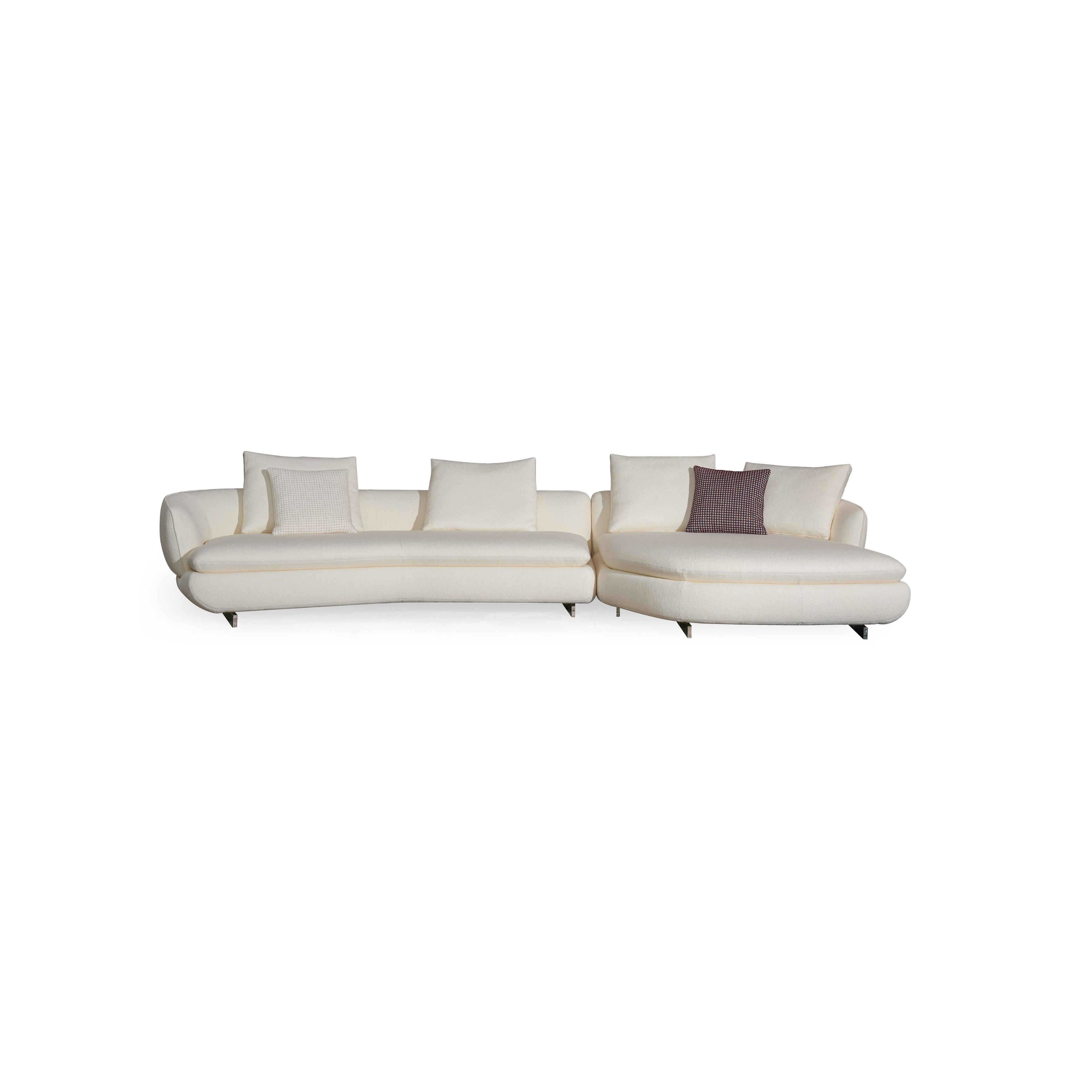 Modern sectional sofa with off-white fabric upholstery, curved backrest, padded armrests, and low-profile metal legs. Features multiple cushions, including one with a textured pattern. Designed for seating and lounging. Category: furniture/sofas
