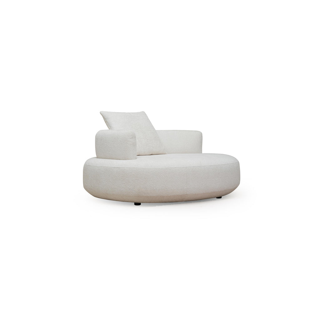 This is a round lounge chair with a single cushioned backrest and one armrest, upholstered in a light beige textured fabric. It rests on four small black legs. Designed for seated relaxation, it features a continuous curved seat and a matching pillow. Category: Furniture > Sofas & Chairs > Lounge Chairs