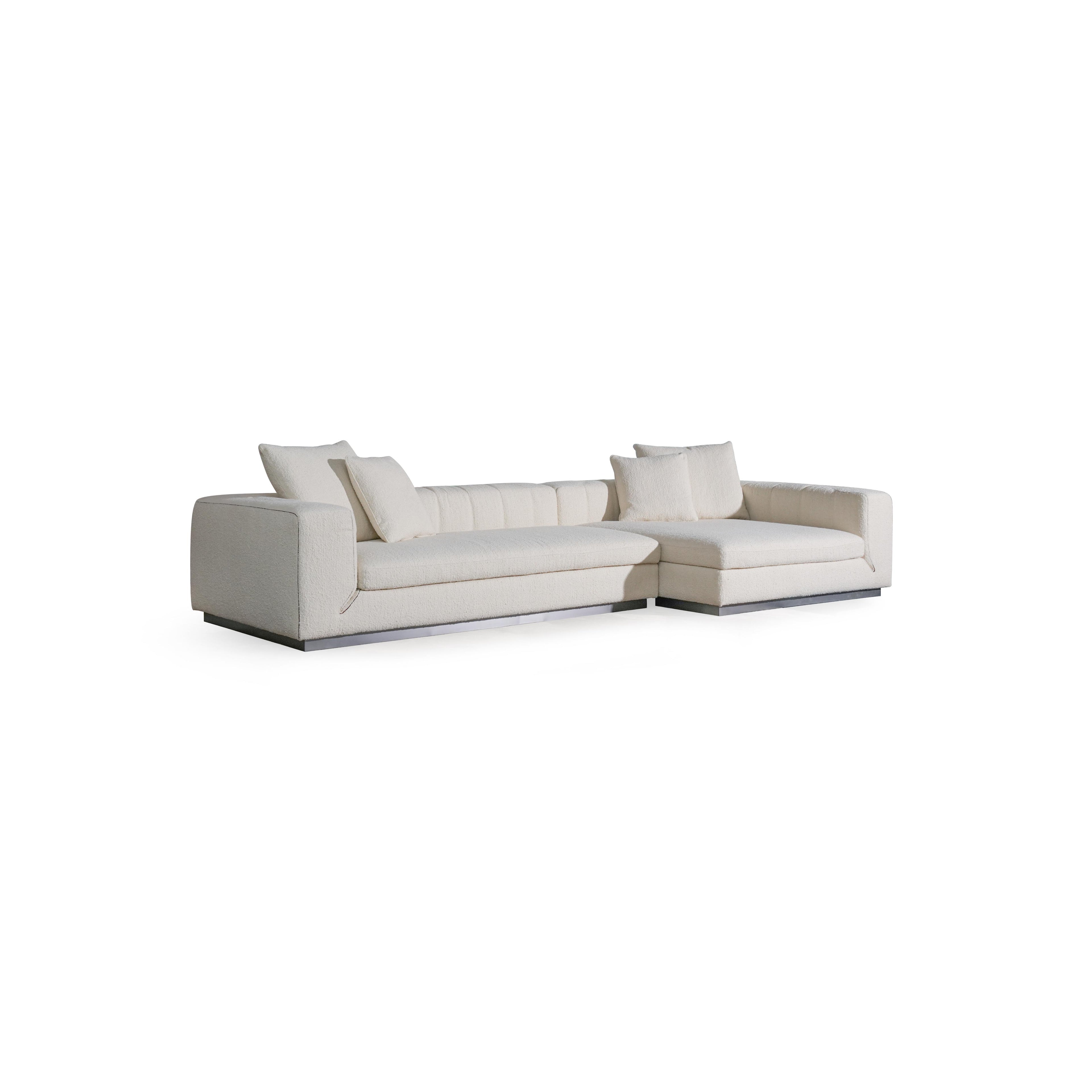 L-shaped sectional sofa with off-white textured fabric upholstery, featuring padded backrest, cushioned arms, and low-profile metal base. Includes multiple throw pillows. Designed for seating and lounging. Category: furniture/sofas