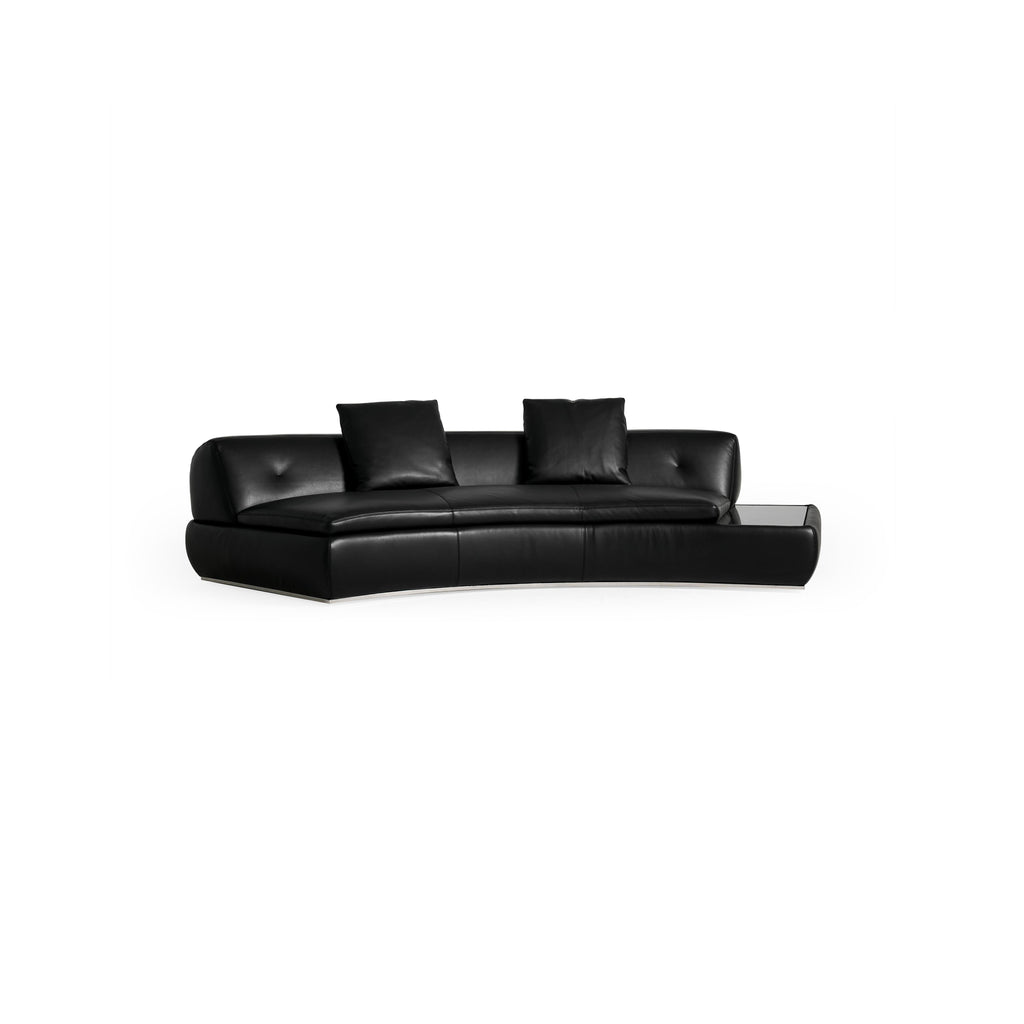 Modular sectional sofa with light gray fabric upholstery, featuring multiple cushioned seating sections, low-profile arms, and a central coffee table with a dark surface. Designed for lounging, it includes visible seam lines and soft, rounded contours. Category: furniture/sofas