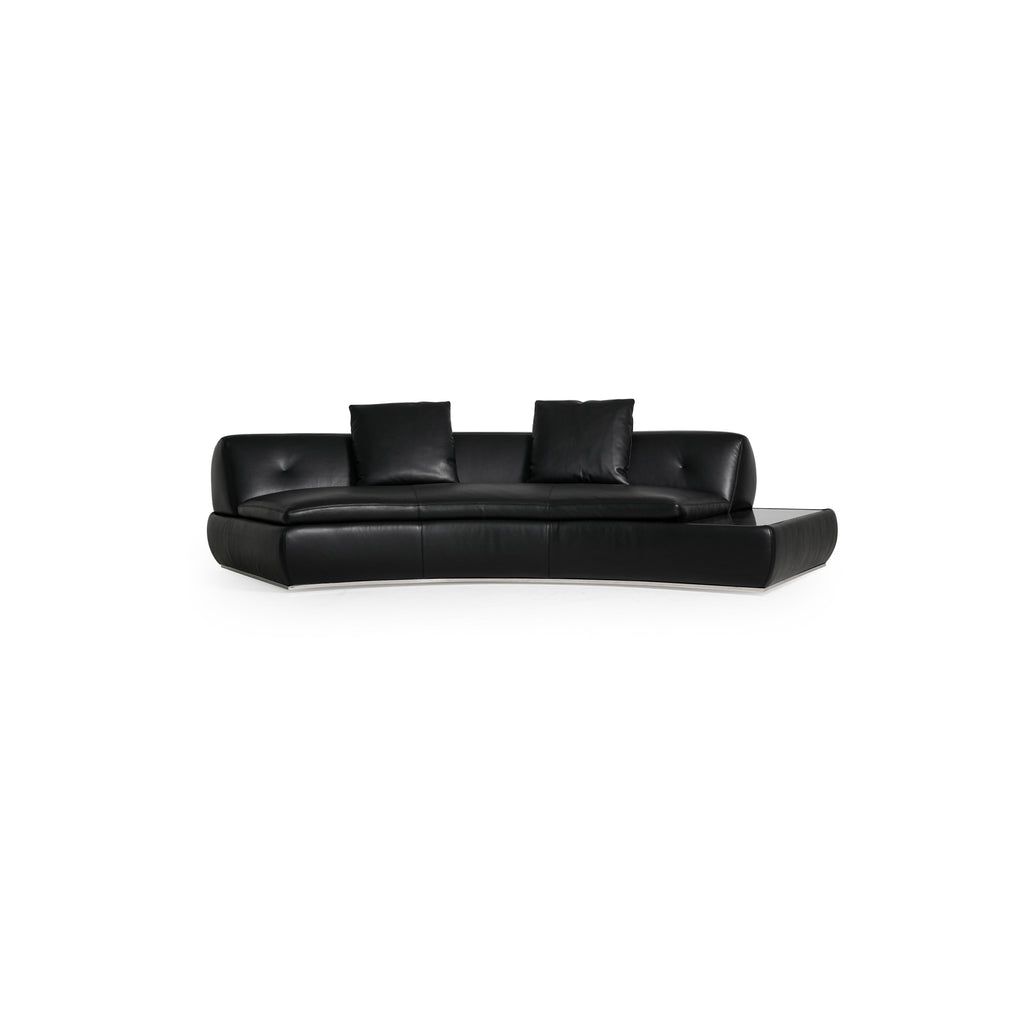 Modular sectional sofa with light gray fabric upholstery, featuring multiple cushioned seating sections, low-profile arms, and a central coffee table with a dark surface. Designed for lounging, it includes visible seam lines and soft, rounded contours. Category: furniture/sofas